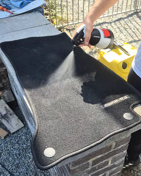 Een hand spuit reiniger op een zwarte automat die op een stenen muurtje ligt in de zon